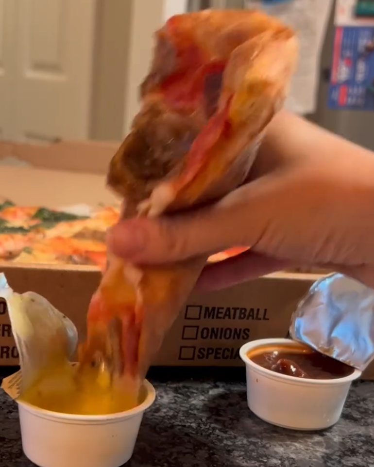 A hand dipping a slice of pizza into sauce.