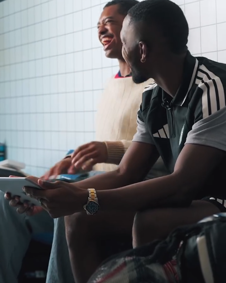 2 NYCFC players sitting next to each other and laughing. One is holding a tablet.